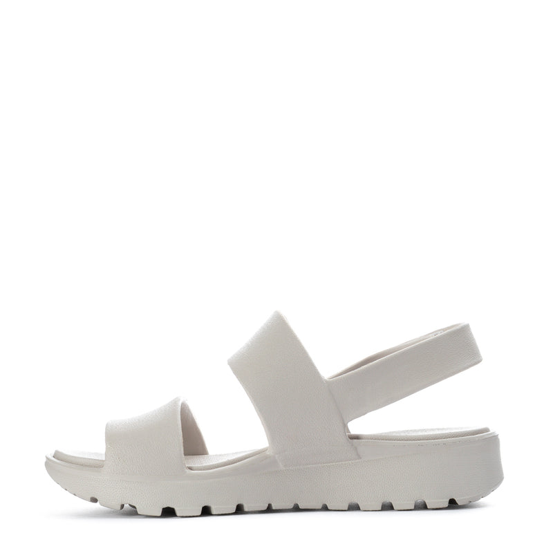 Women’s foam slide sandal, side view, light neutral straps and textured rubber sole
