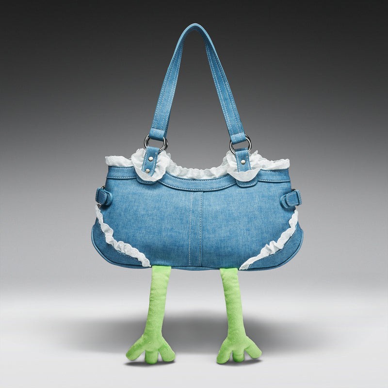 Blue denim handbag with white lace trim and green frog legs on a gray background