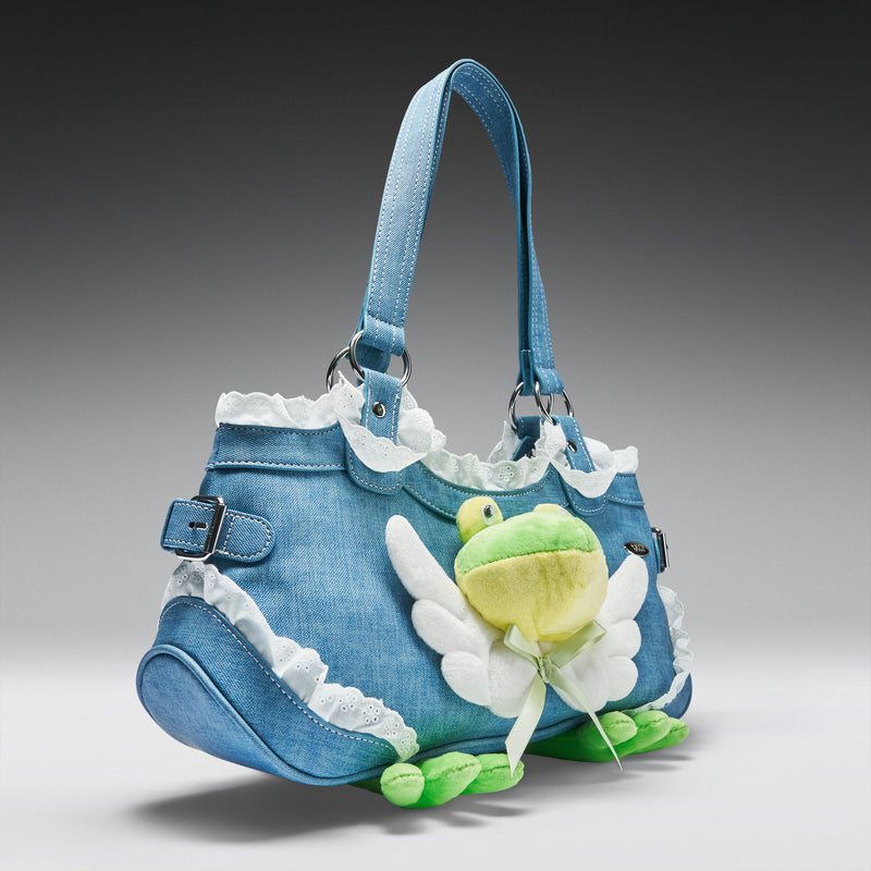 Blue denim handbag with a green frog charm on a gray background