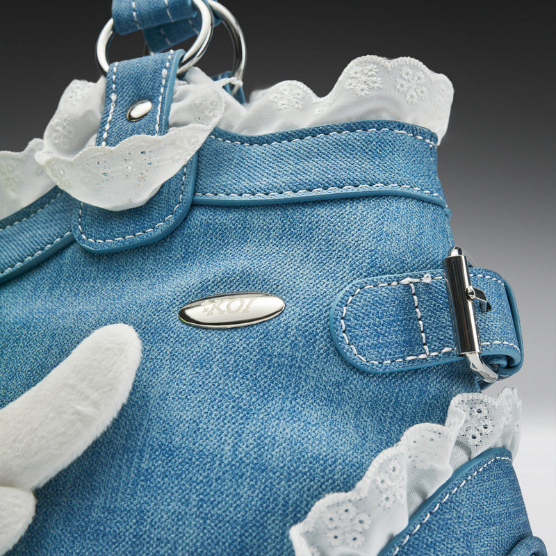 Close-up of a blue denim dog dress with white lace details on a gray background