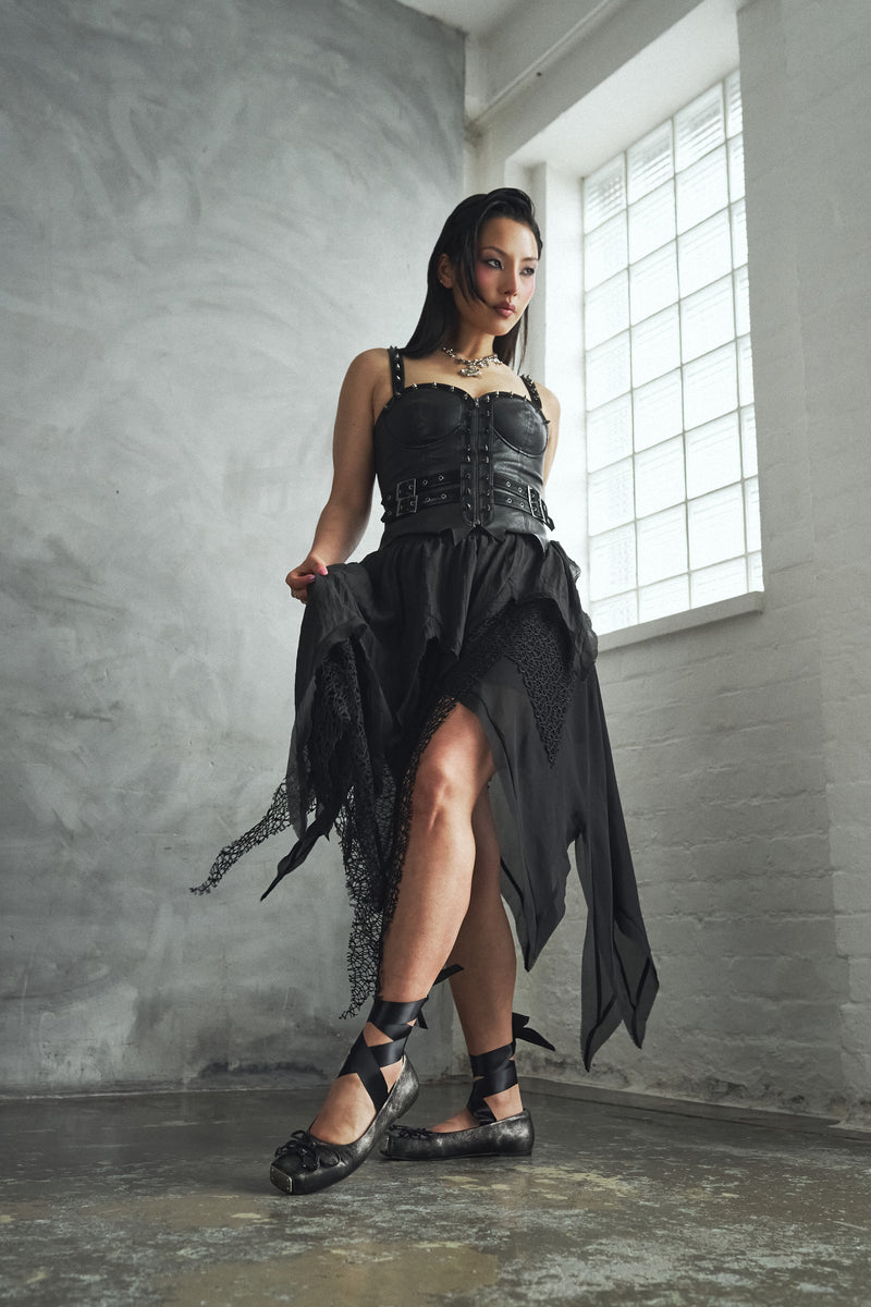 Woman in a black dress standing in a room with large windows.