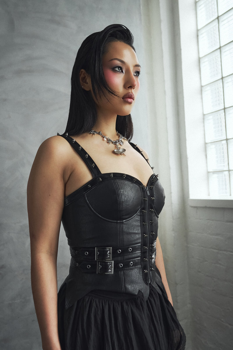 Woman wearing a black leather outfit with a corset-style top in a softly lit room.