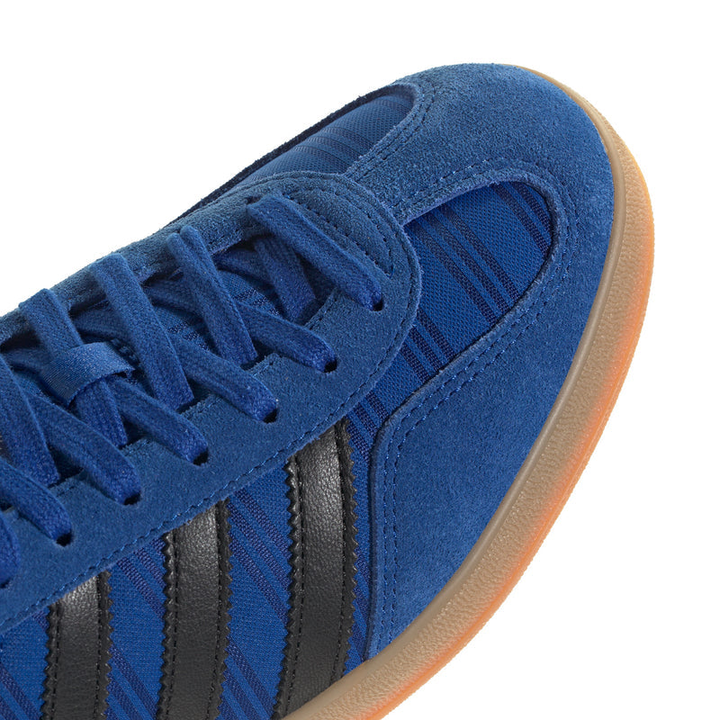 Blue suede indoor sneaker close-up with laces and black three stripes