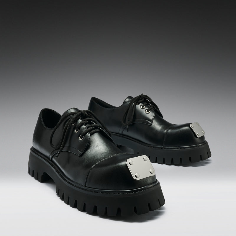 Black leather shoes with silver accents on a gray background