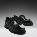 Black leather shoes with silver accents on a gray background