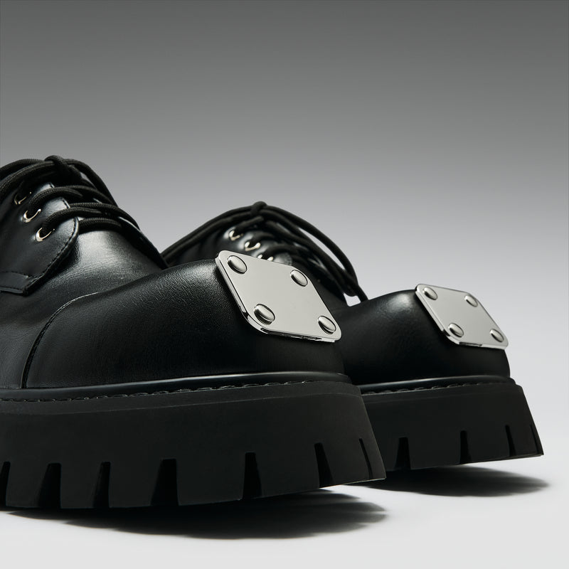 Black platform shoes with silver buckles on a gray background