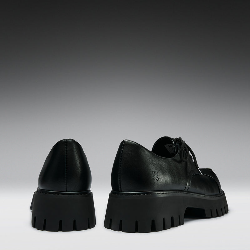 Black leather shoes with thick soles on a gradient gray background