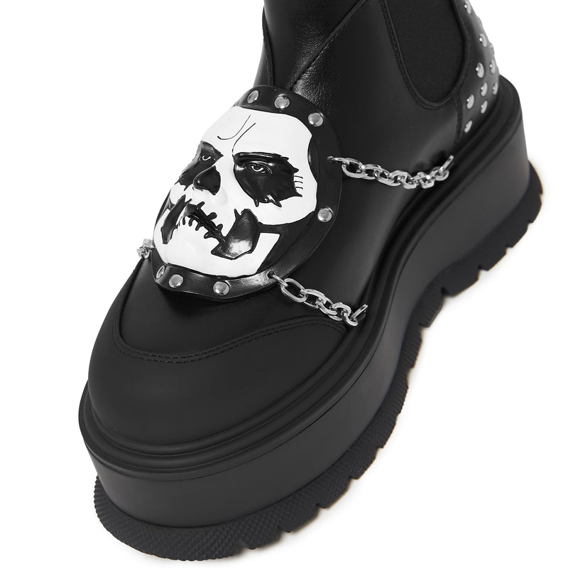 Detail of a black platform boot with studs and chain detail on a white background
