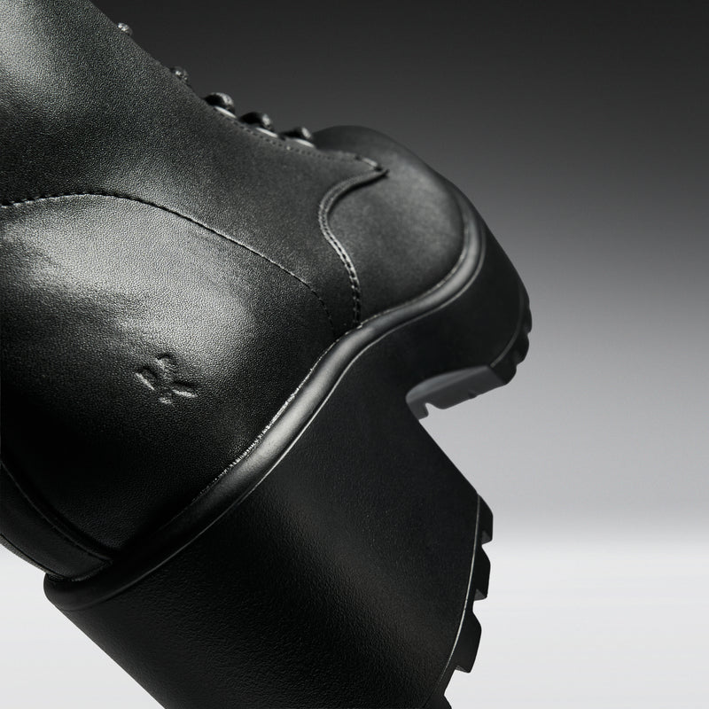 Close-up of a black leather boot on a gradient background
