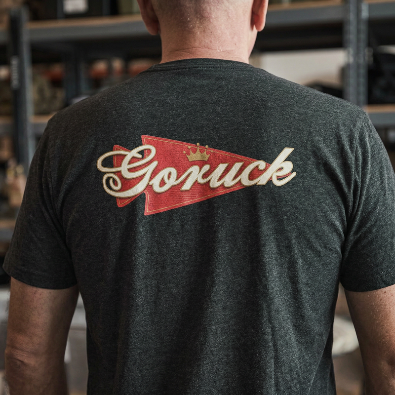 Man wearing the GORUCK Bud Tee - Tri-BlendX, featuring a bold red and gold "Goruck" logo on the back. Ideal for everyday wear and comfort indoors.