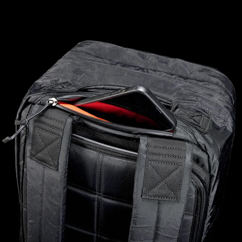 GORUCK black rucksack with visible padded straps and zippered pocket open to reveal a phone