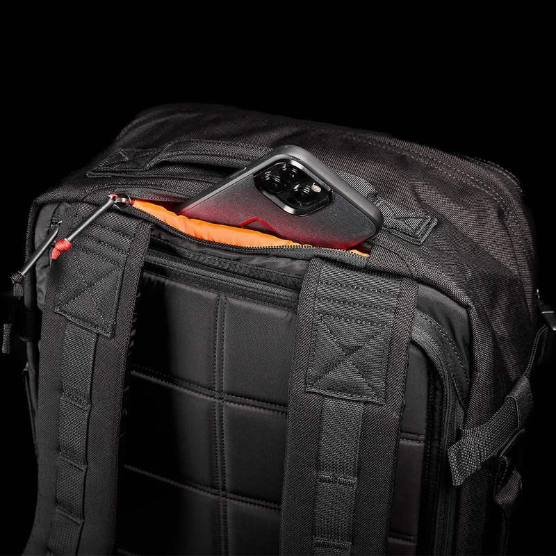 GORUCK black rucksack with padded straps, rear zip pocket open showing a smartphone inside