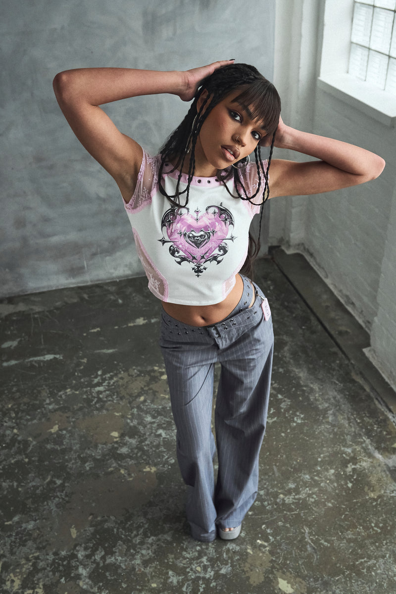 Person wearing a white crop top with a graphic design and gray pants in an industrial setting.