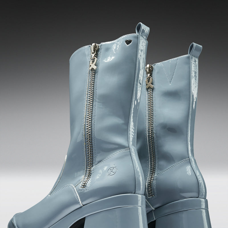 Pair of light blue patent leather boots with zippers on a gradient background