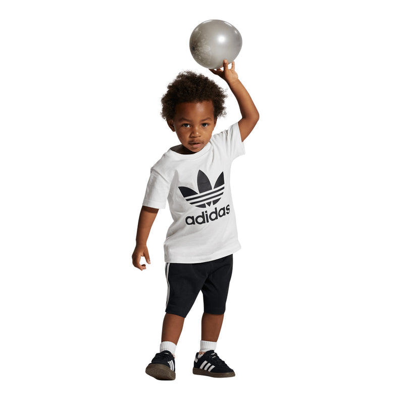 Toddler wearing a white adidas logo T-shirt, black shorts, and black sneakers with stripes.