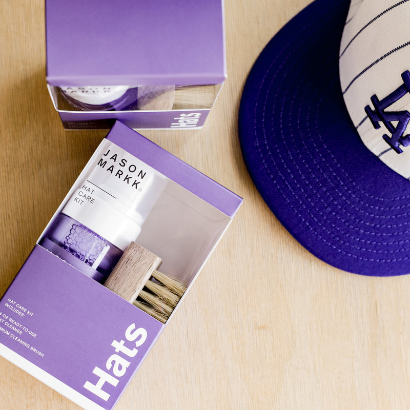 Hat care kit with cleaner bottle and wooden bristle brush beside purple cap