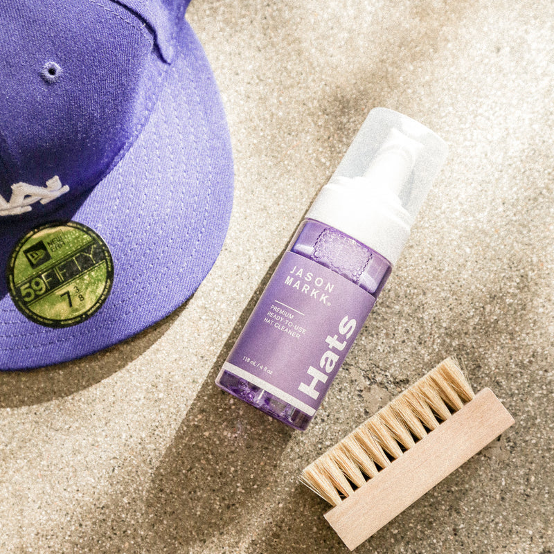 Jason Markk hat cleaner with purple cap and wooden bristle brush on concrete