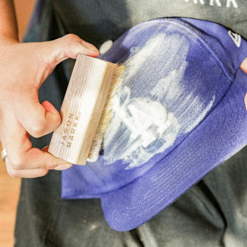 Hand scrubbing a purple cap with a wooden bristle cleaning brush