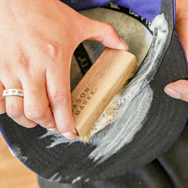 Hand scrubbing a dark cap with a wooden bristle cleaning brush