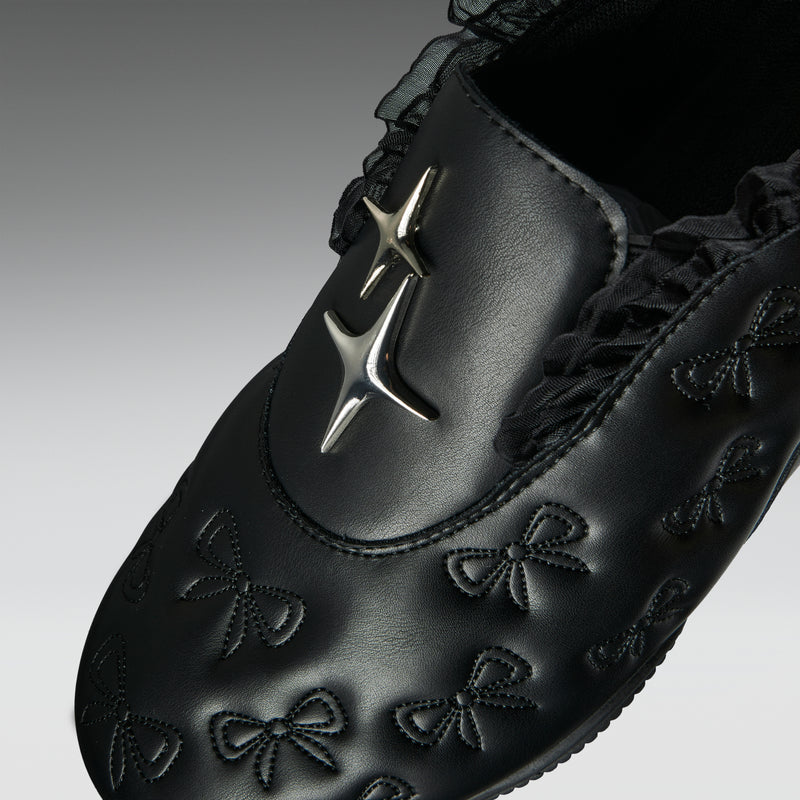 Black shoe with decorative patterns and a star emblem on a gray background