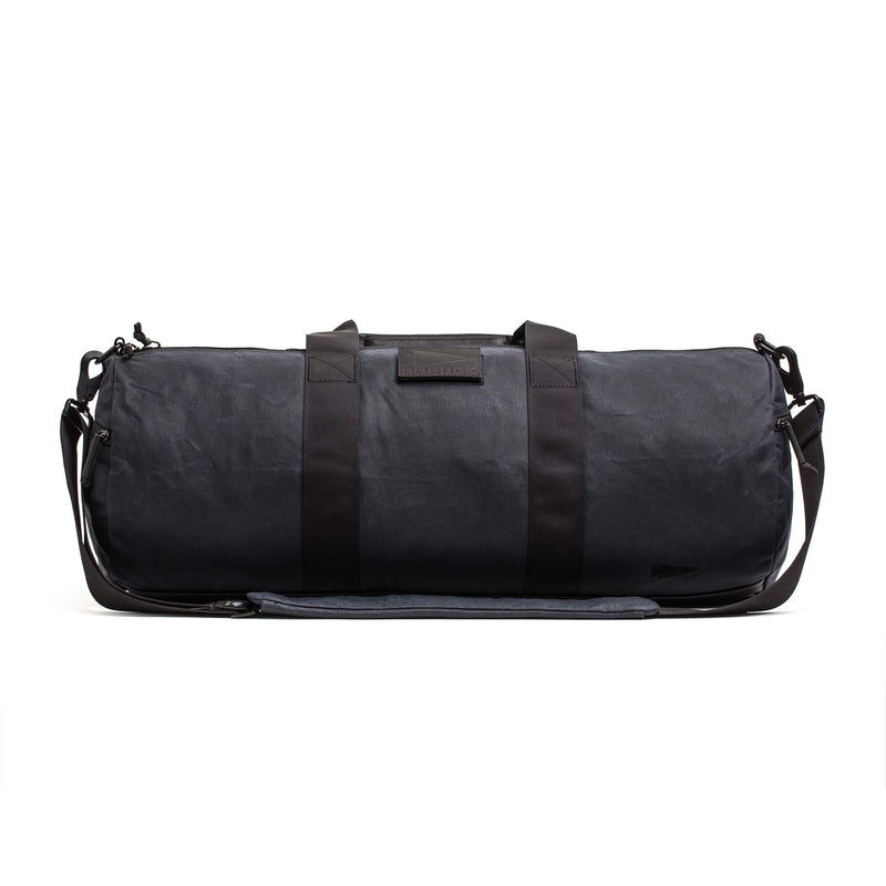 The Gym Bag - Waxed Canvas features classic black waxed canvas, two handles, a shoulder strap, and a minimalist design, all set against a white background.
