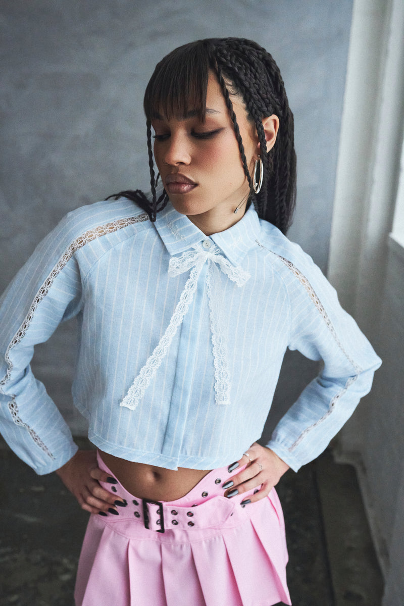 Woman wearing a light blue embroidered blouse and pink skirt against a gray background