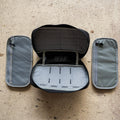 The IFAK (Black + Red Thread + Grey Interior + Red Patch) ROBIC w/ Aquaguard is open to show its gray pouches on each side, displayed on a textured beige surface.
