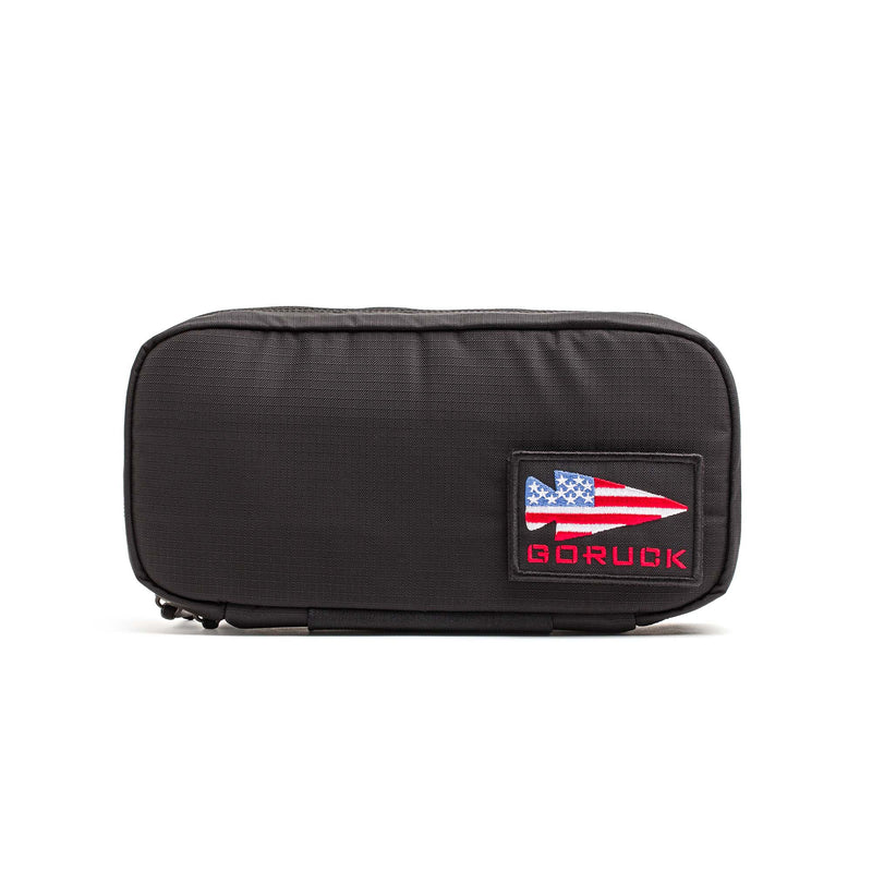 The GORUCK IFAK is a black zippered pouch featuring a patch with a U.S. flag arrow and "GORUCK" text, ideal for use as a tactical medical pouch or Individual First Aid Kit.
