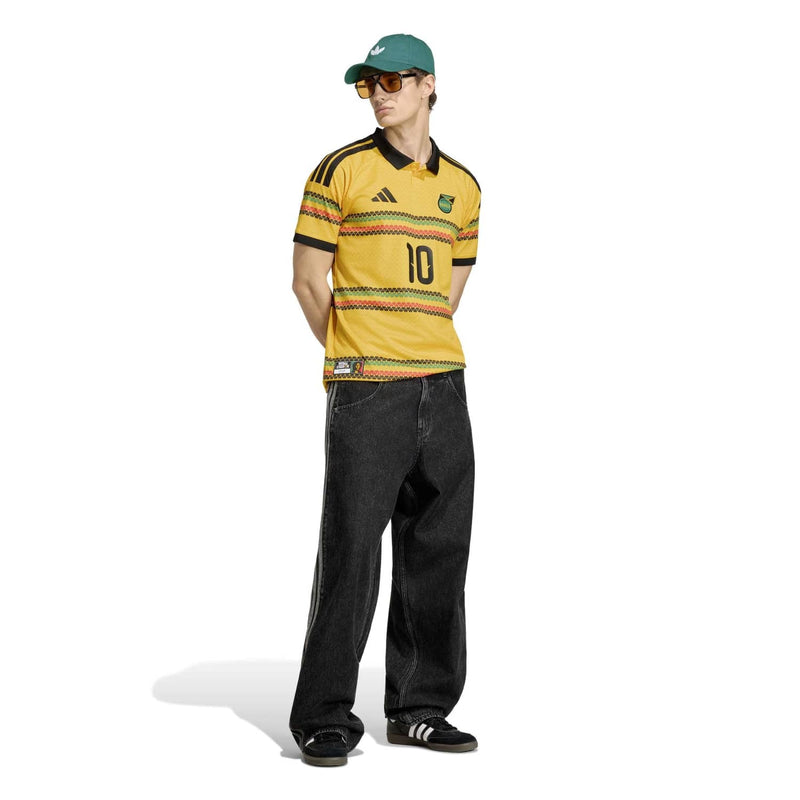 Men's yellow soccer jersey with patterned stripes and black trim, worn with dark jeans