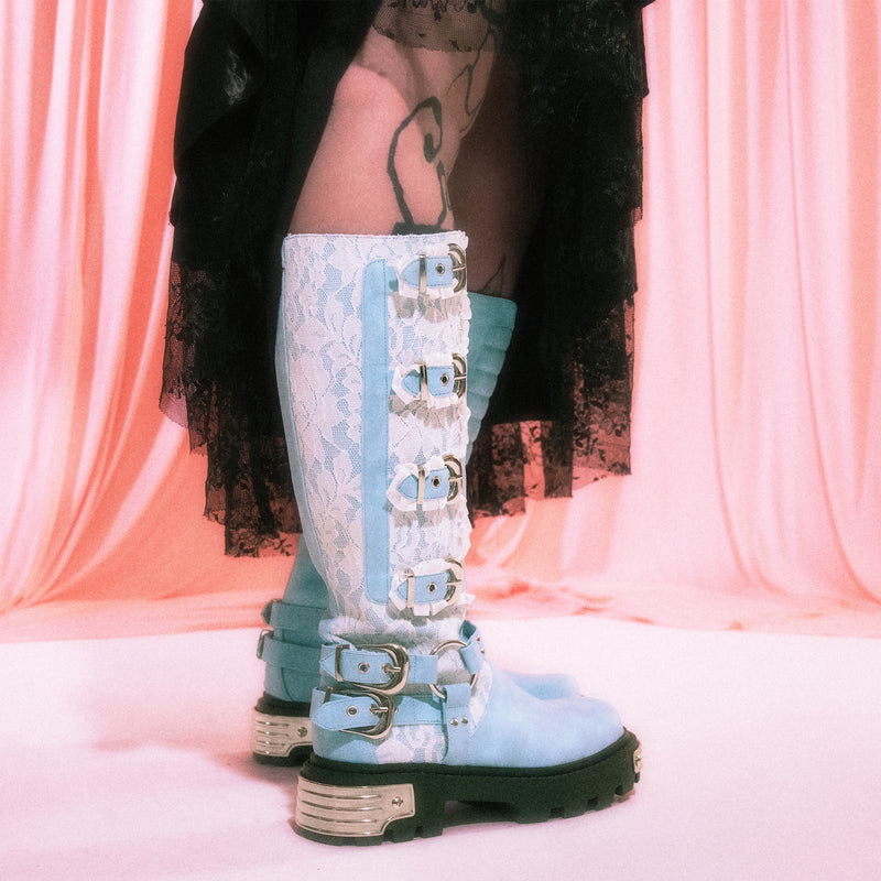 Light blue knee-high boots with decorative straps on a pink curtain background