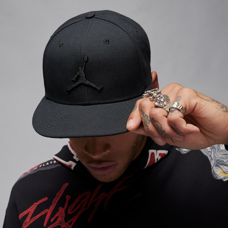 Black snapback cap being adjusted by model hand; Jumpman logo visible.