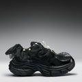 Black sneaker with textured design and pearl embellishments on a gray background