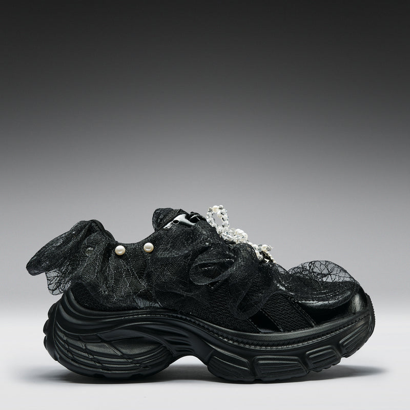 Black sneaker with textured design and pearl embellishments on a gray background
