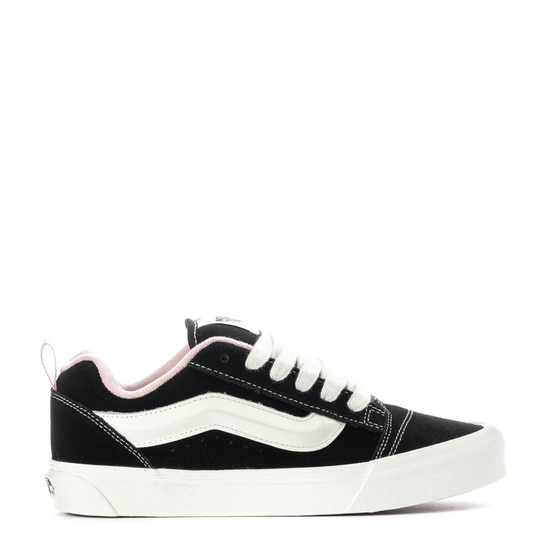 Black low-top sneakers with white side stripe and pink accents, lace-up.