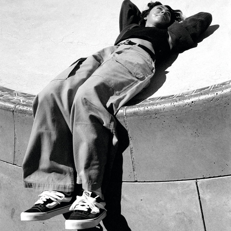 Low-top black and white sneakers with white laces, worn and resting on pavement