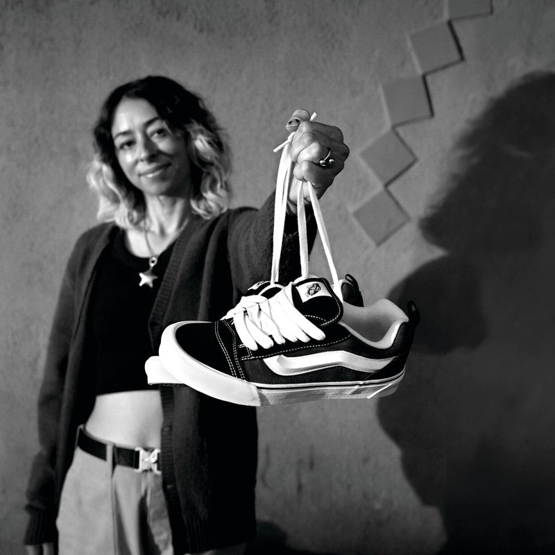 Black and white low-top sneakers held up by a hand, lace-up with white side stripe