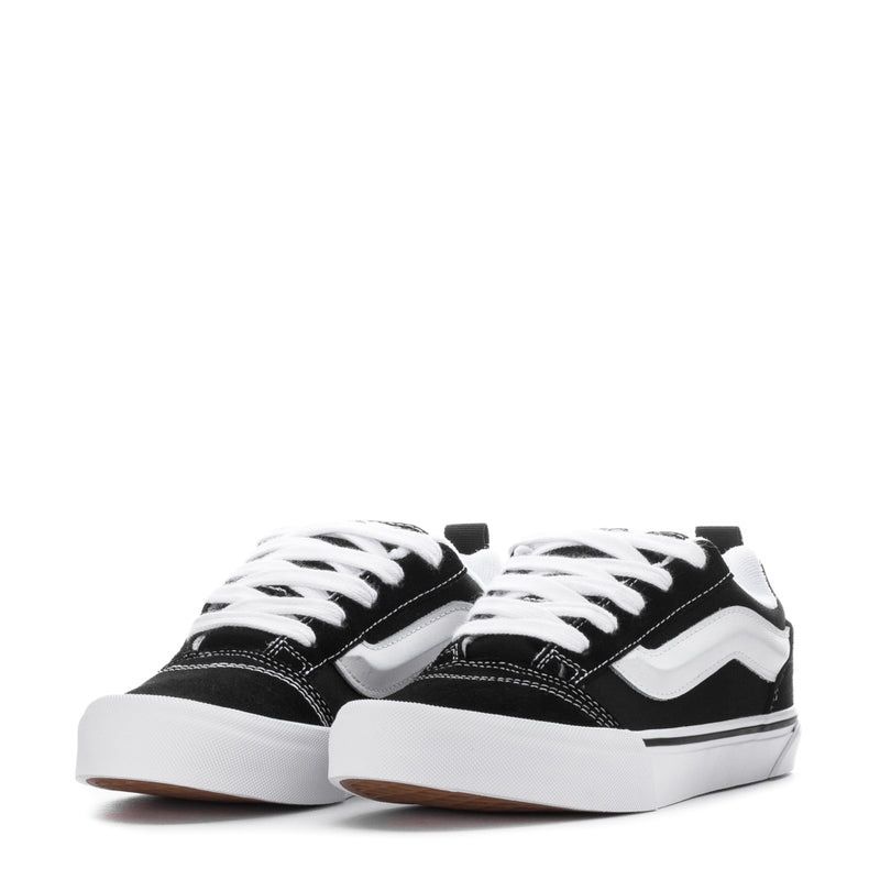 Pair of black youth lace-up sneakers with white wavy side stripe and thick white sole.