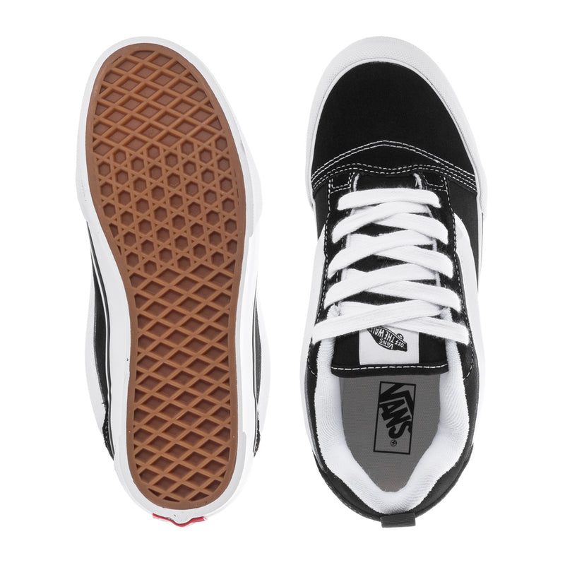 Black and white youth sneakers showing treaded gum outsole and lace-up tongue.