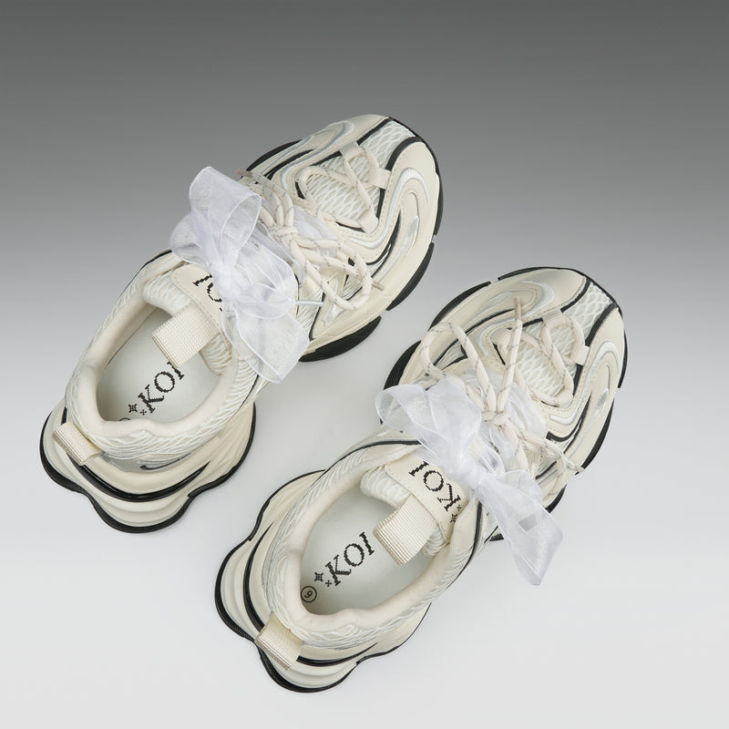 White sneakers with black accents and decorative ribbons on a gray background