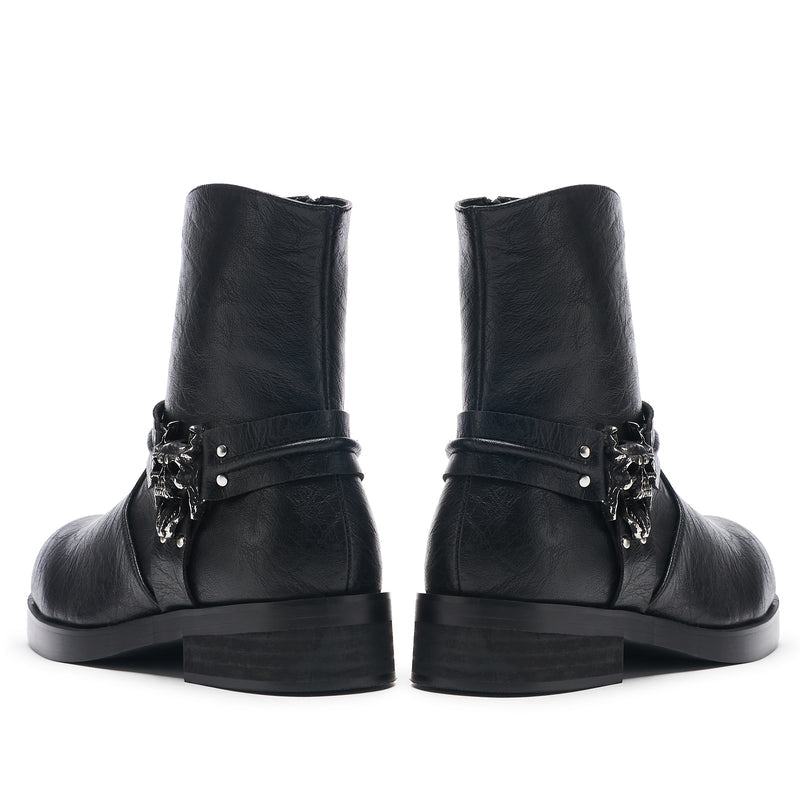 A pair of vintage black leather biker boots with stacked hardware and a decorative element on the heel.