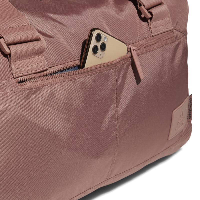 Warm clay pink duffel bag with zip pocket holding a smartphone