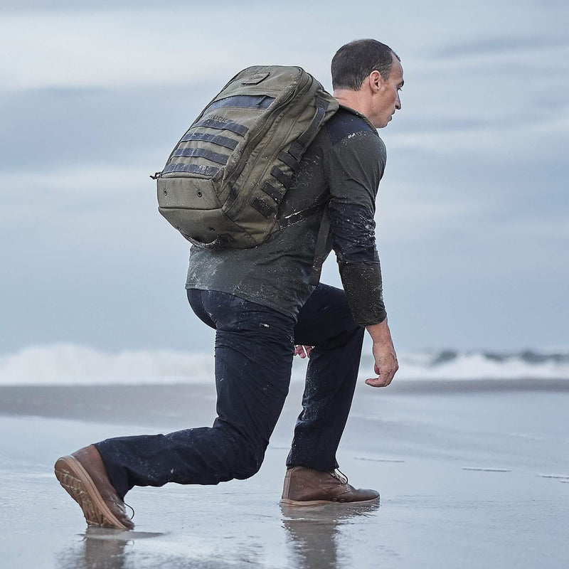 Man rucking on wet beach with GORUCK backpack, rugged gear, training by the ocean