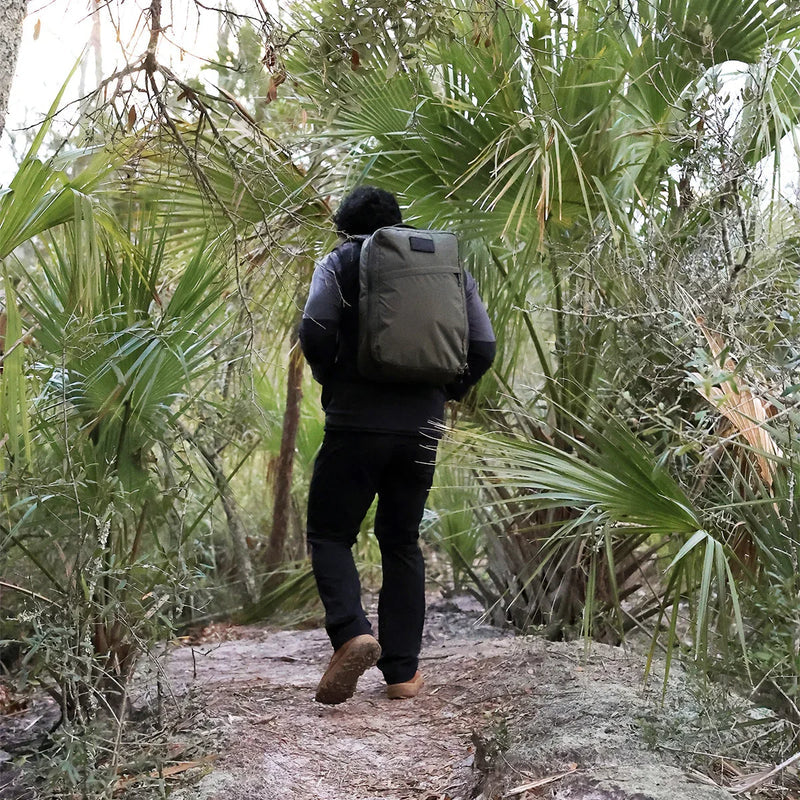 Person rucking with a GORUCK backpack on a forest trail, surrounded by green palm trees.