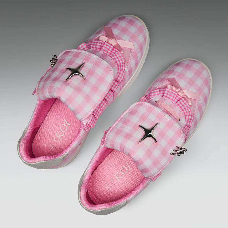 Pink checkered slippers with decorative bows and a brand logo on a light gray background