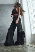 Person wearing a black outfit with feathered details in a room with large windows.