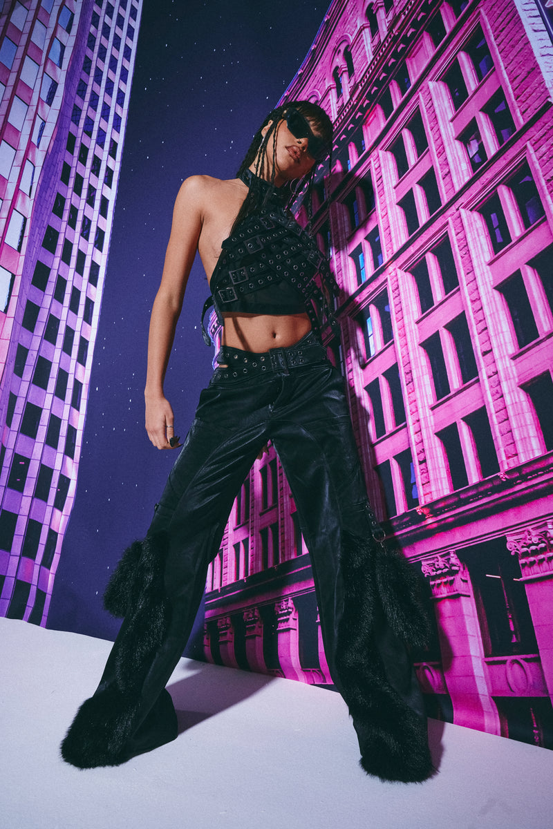 Person wearing a black outfit with fur details against a stylized cityscape background