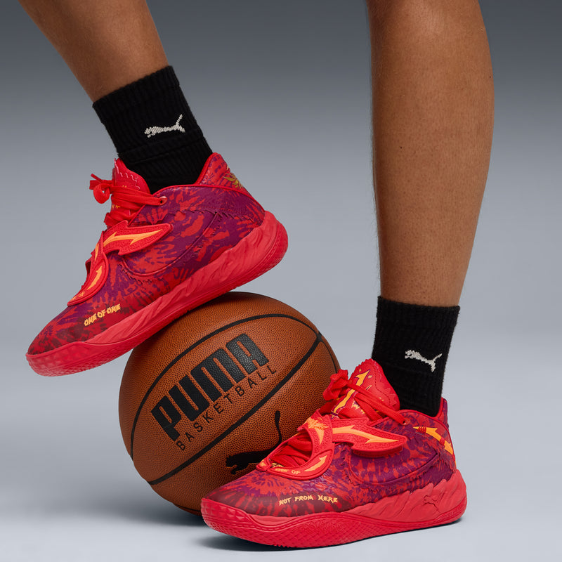 Red low-top basketball sneakers on model with black socks, beside basketball, side view.
