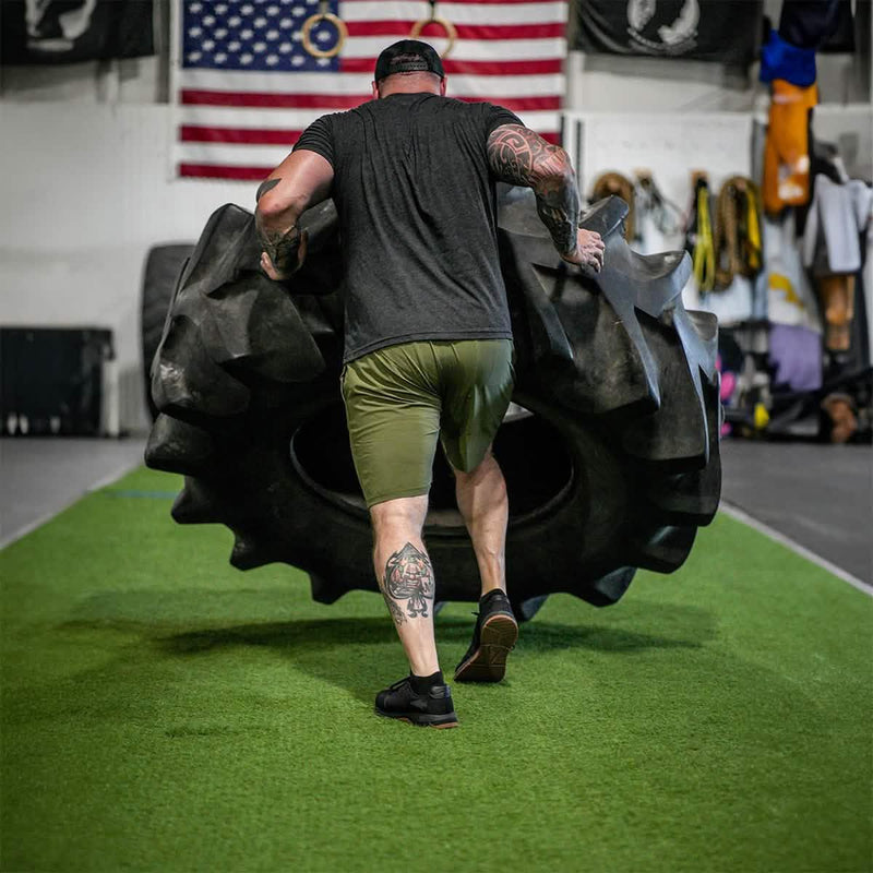 Man flipping large tire in gym with American flag, showcasing GORUCK rucking strength training