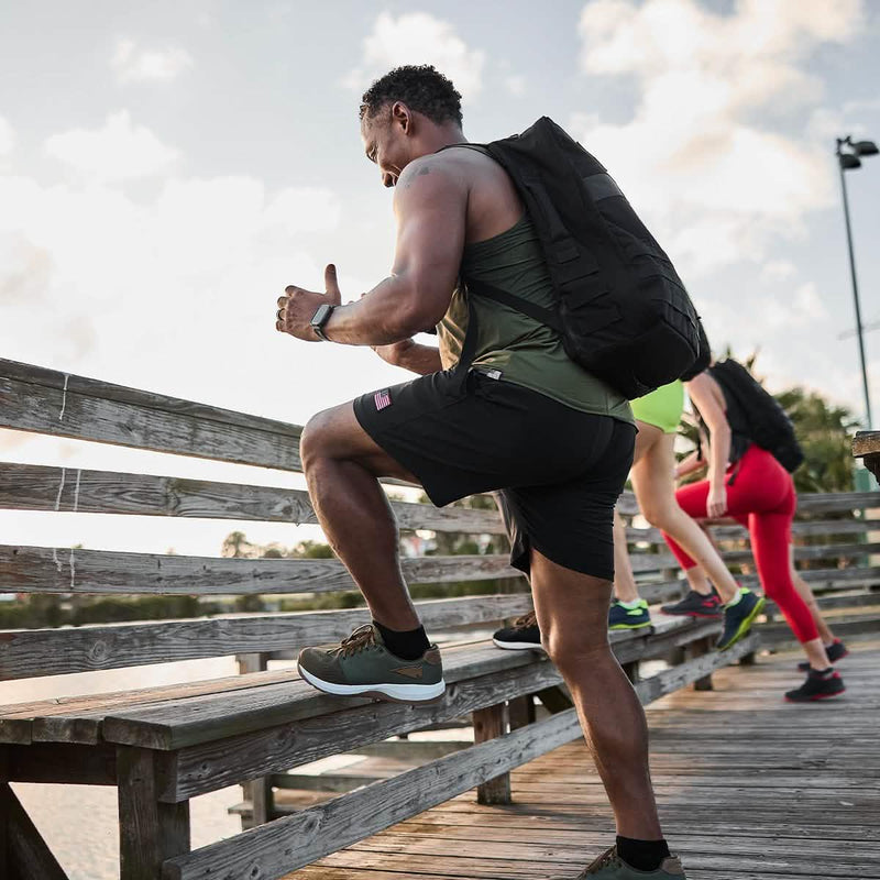 Man rucking on wooden bridge wearing GORUCK gear and backpack, leading fitness group outdoors