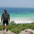 Man wearing GORUCK black Challenge Shorts and backpack overlooking a scenic beach